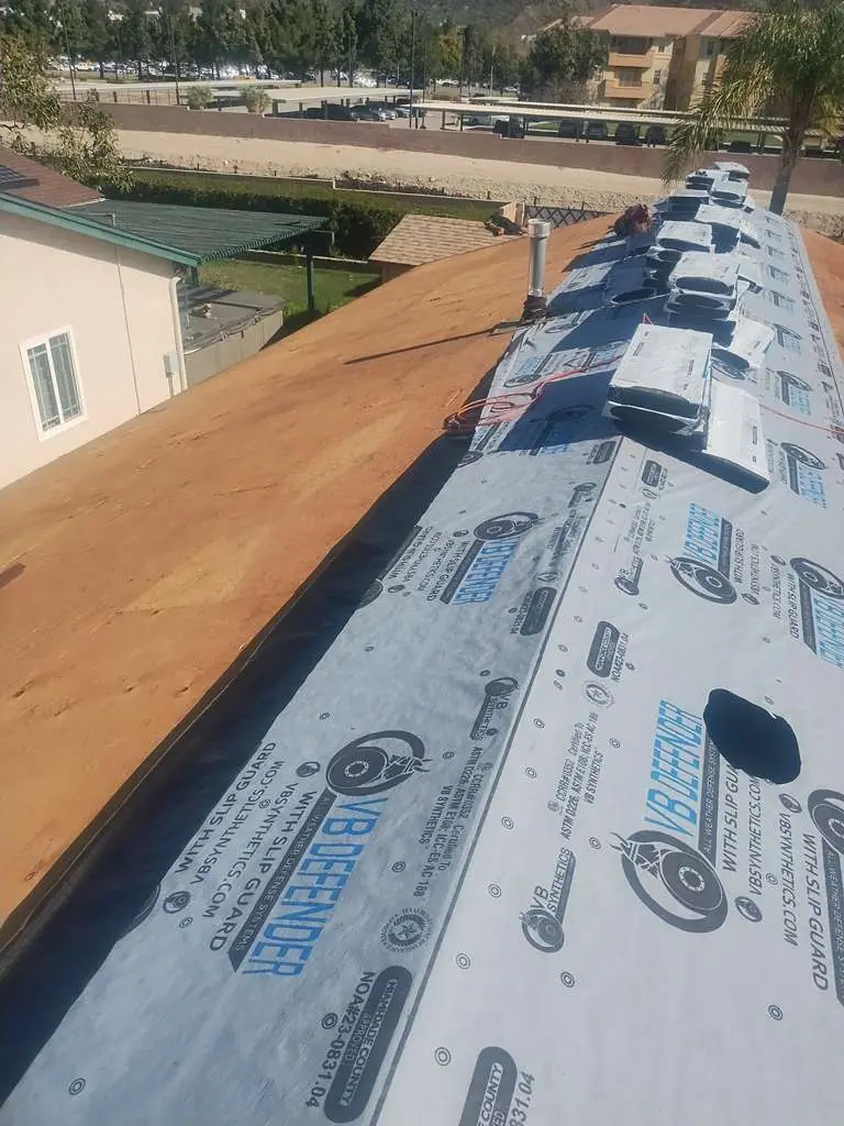 Printed underlayment and staged material along a roof ridge beside exposed wood decking