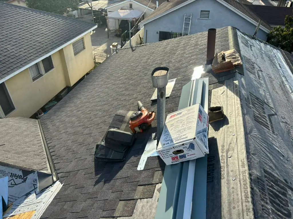 Packaged materials, metal pieces, and tools staged on a shingle roof